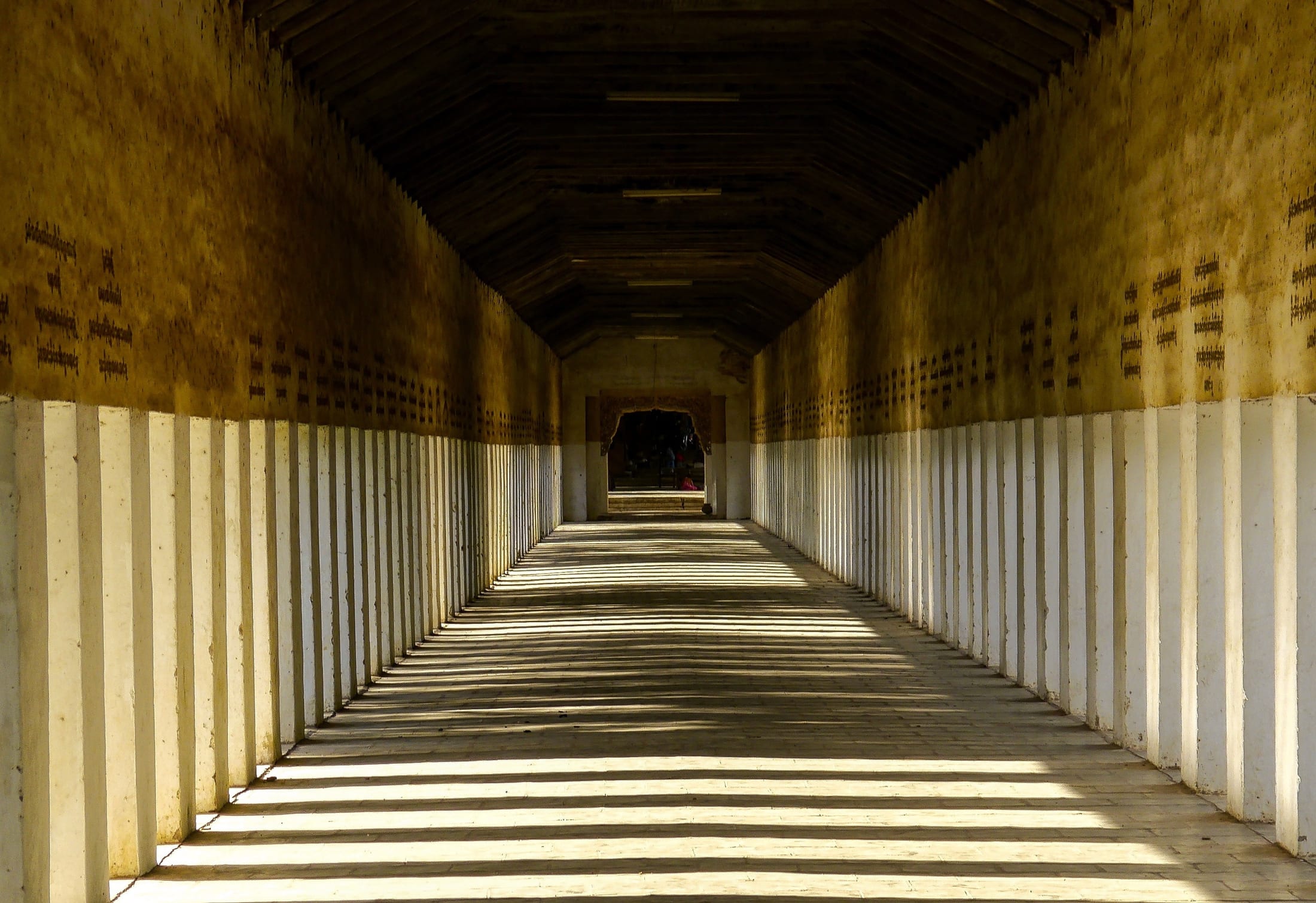 A sunlit teak colonnade inside a Myanmar monastery