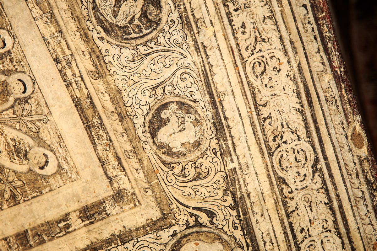 A detailed, centuries-old mural inside Somingyi Kyaung, with painted animal roundels and ornate scrollwork.