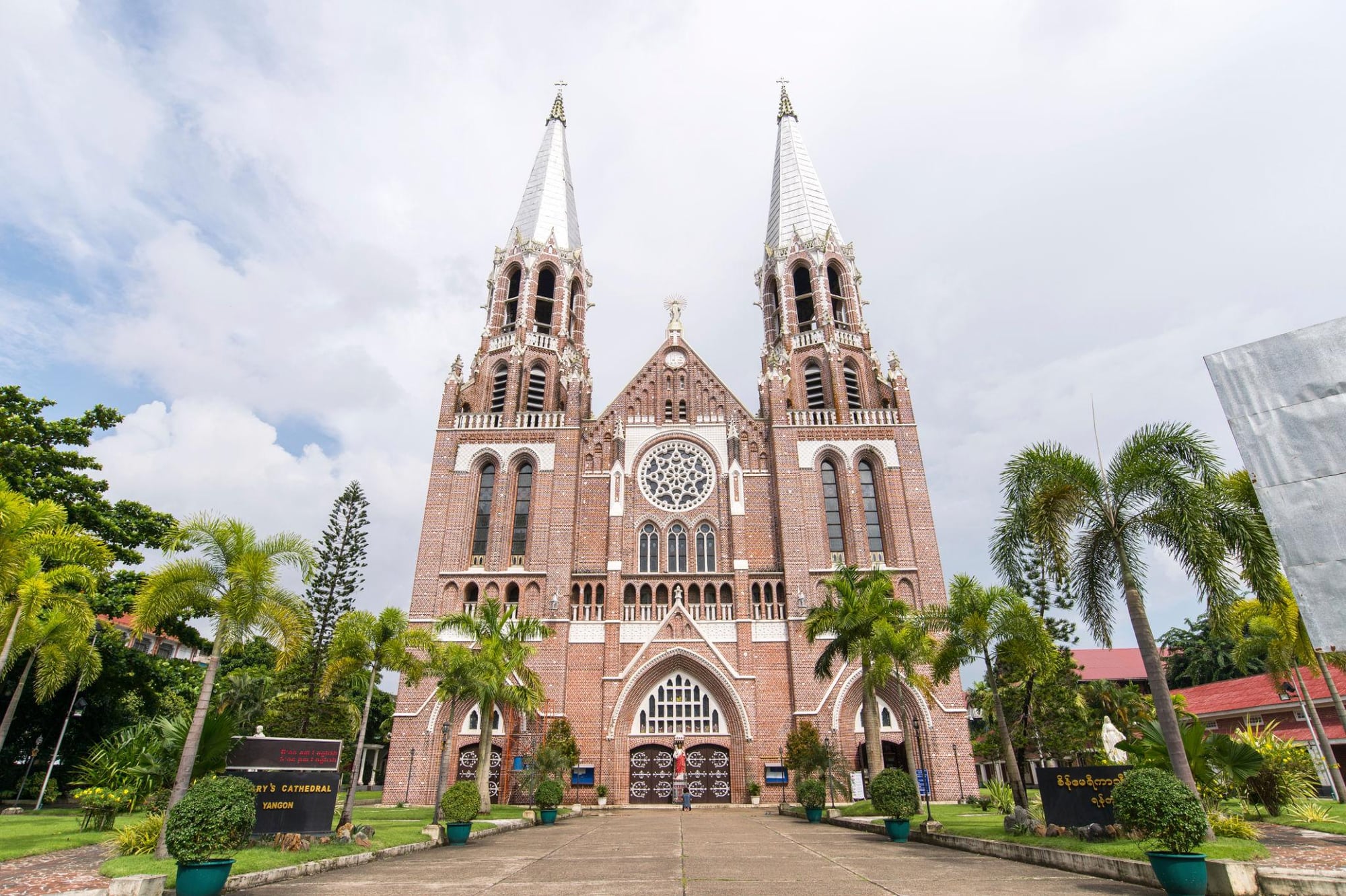 The red-brick Gothic Revival facade of St Mary's Cathedral in Yangon, with its rose window and twin towers framed by palm trees.
