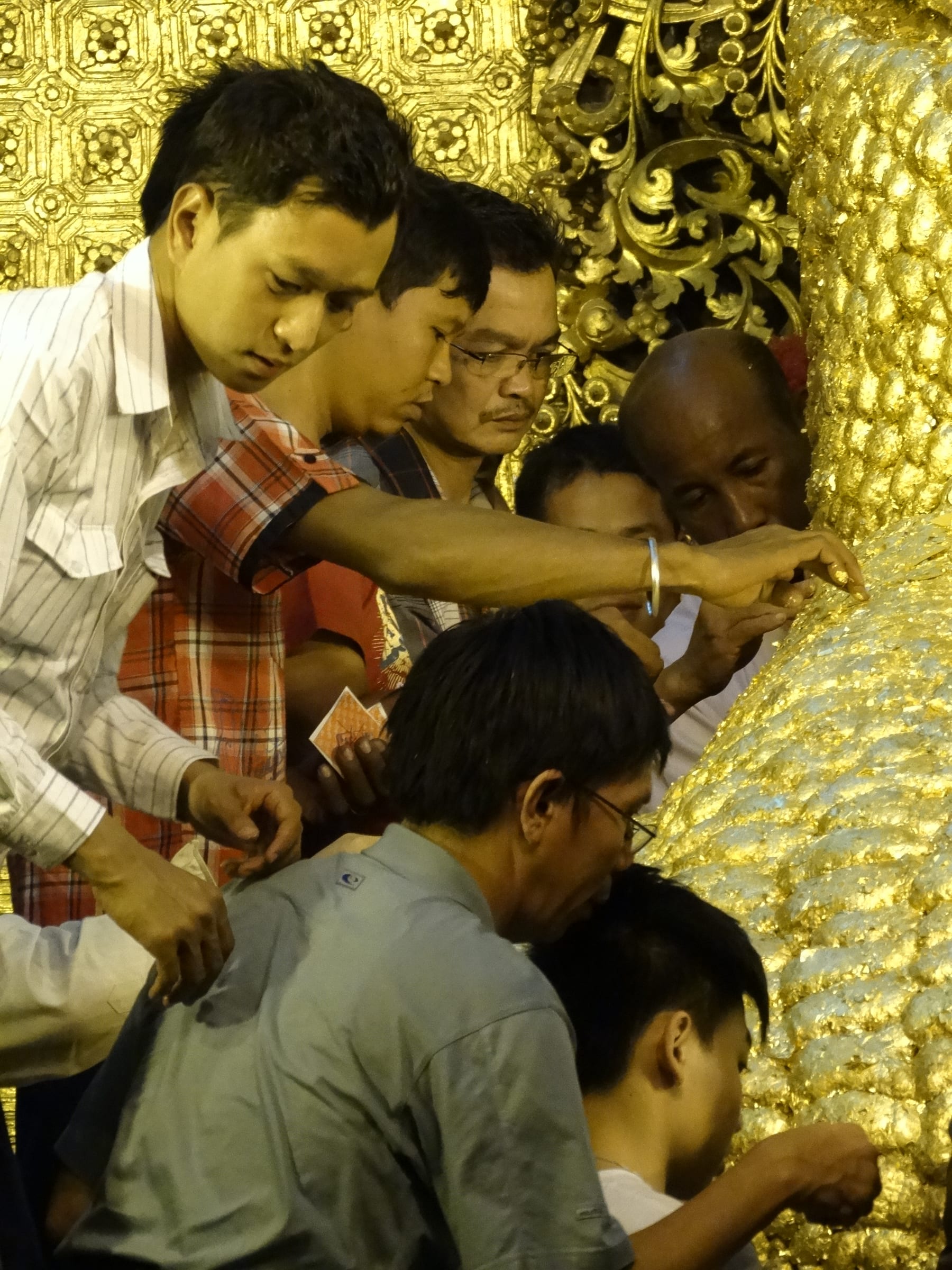 Devotees at Mahamuni Buddha Temple reach forward to press squares of gold leaf onto the thickly gilded surface of the Buddha image.
