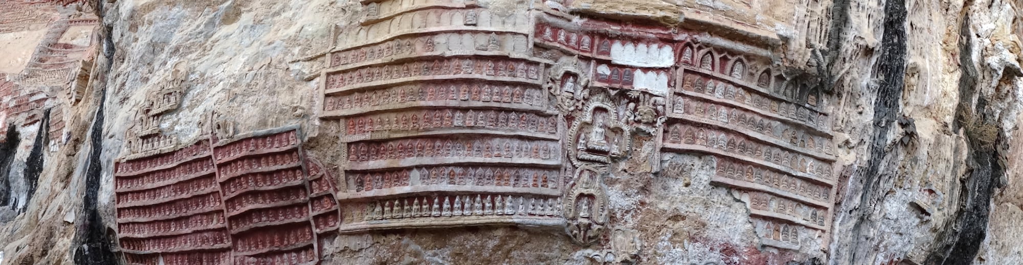 Thousands of small carved Buddha images cover the limestone cliff face of Kawgun Cave in rows.