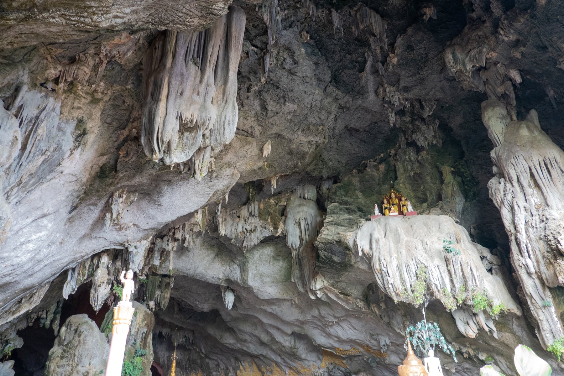 Inside Saddan Cave near Hpa-An, stalactites hang from the ceiling above a small shrine of Buddha images set on a rock ledge.