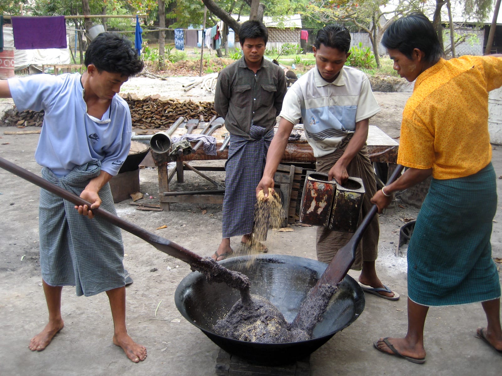 Four men stir a huge wok of glutinous rice, peanuts and sesame with long wooden paddles to make htamane.