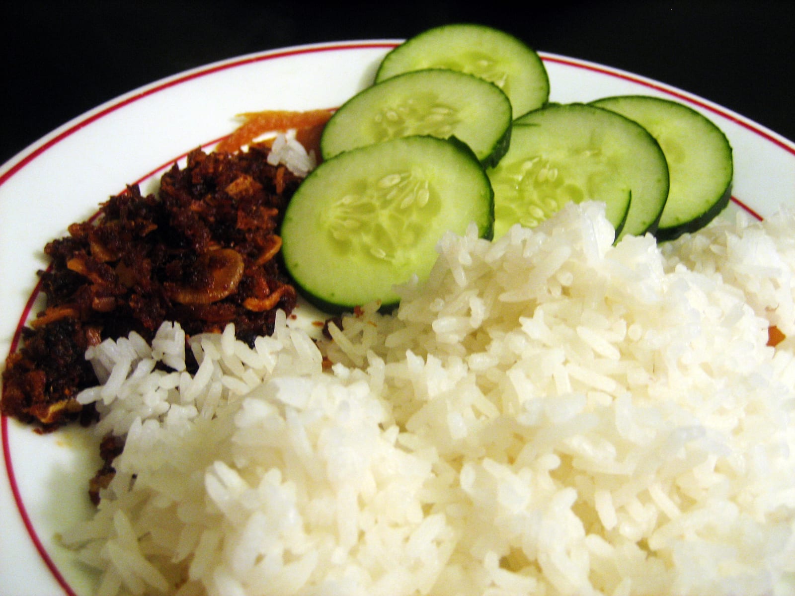 A plate of ngapi kyaw, fried fermented fish paste, served with sliced cucumber and steamed rice.