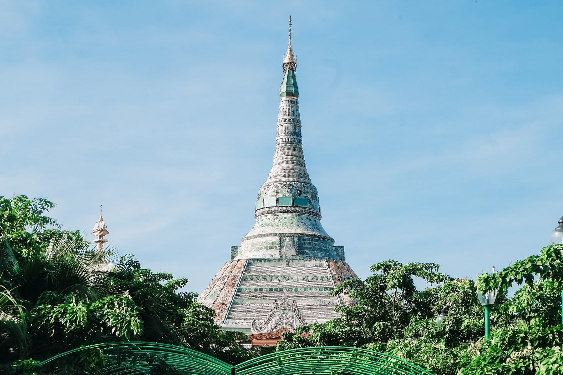 The jade-tiled spire of the pagoda rises above lush green trees against a clear blue sky.