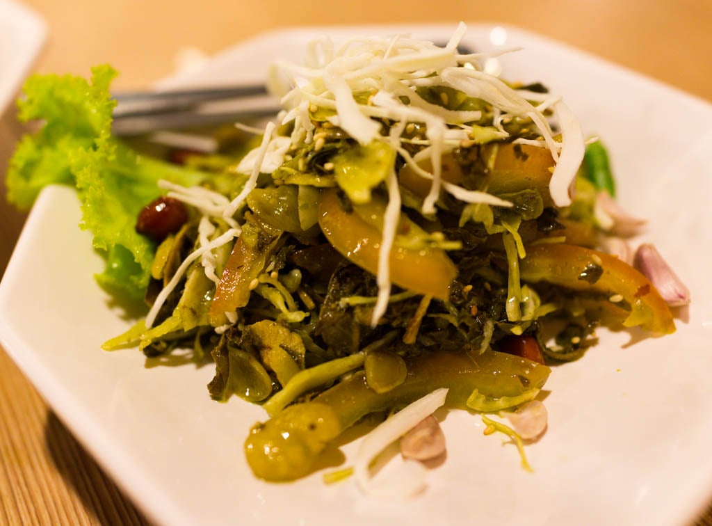 A plate of lahpet thoke, fermented tea leaves mixed with cabbage, tomato, garlic and peanuts.