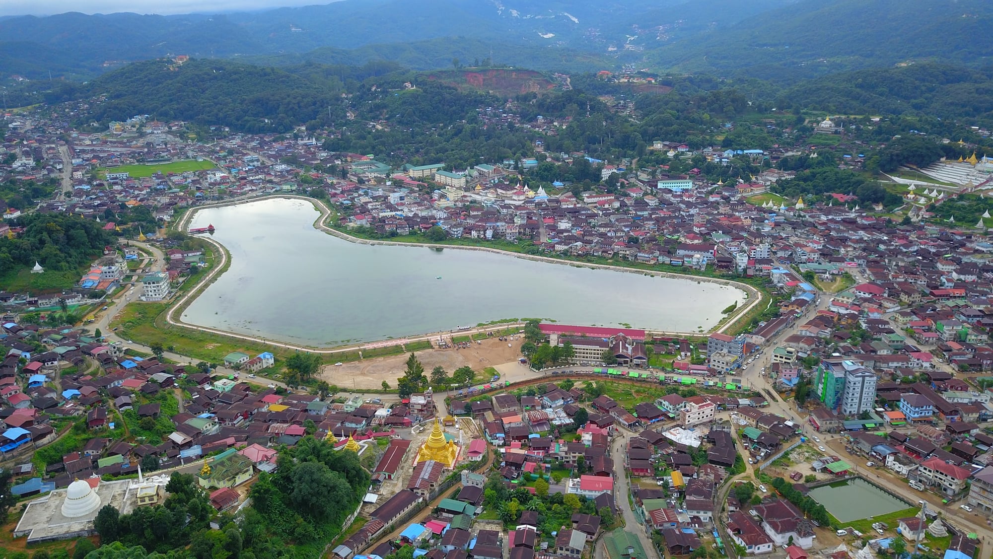 Aerial view of Mogok township in Myanmar, its lake and pagodas surrounded by forested hills.