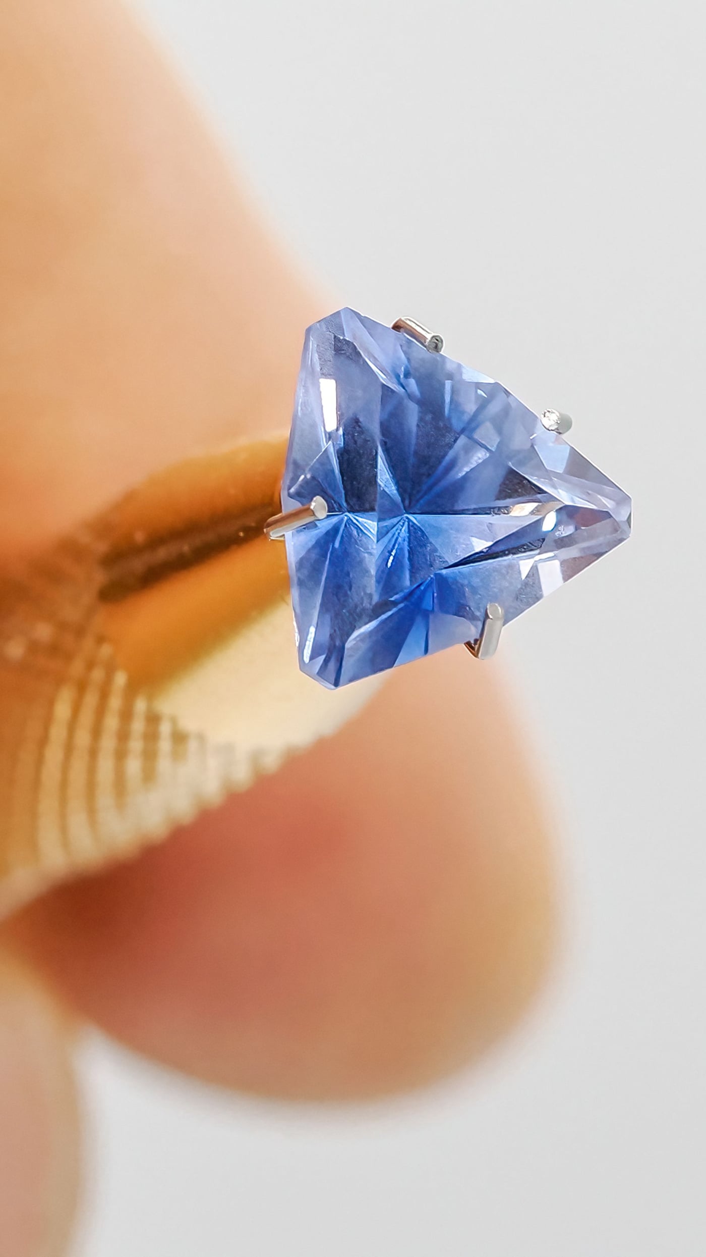 A faceted blue sapphire held delicately in prongs, examined closely against a plain background.