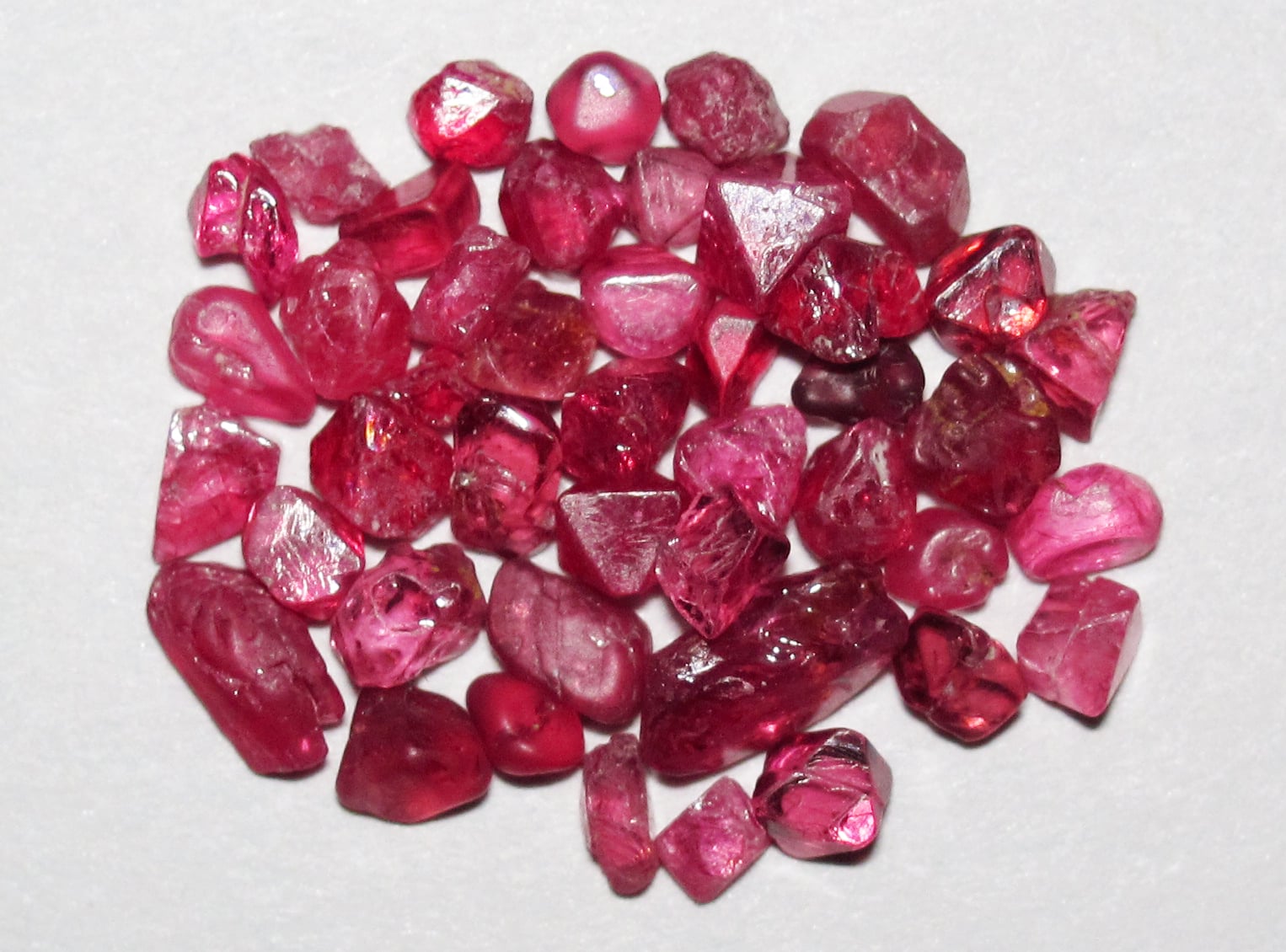 A pile of rough, gemmy pink and red spinel crystals of varying shapes and sizes.