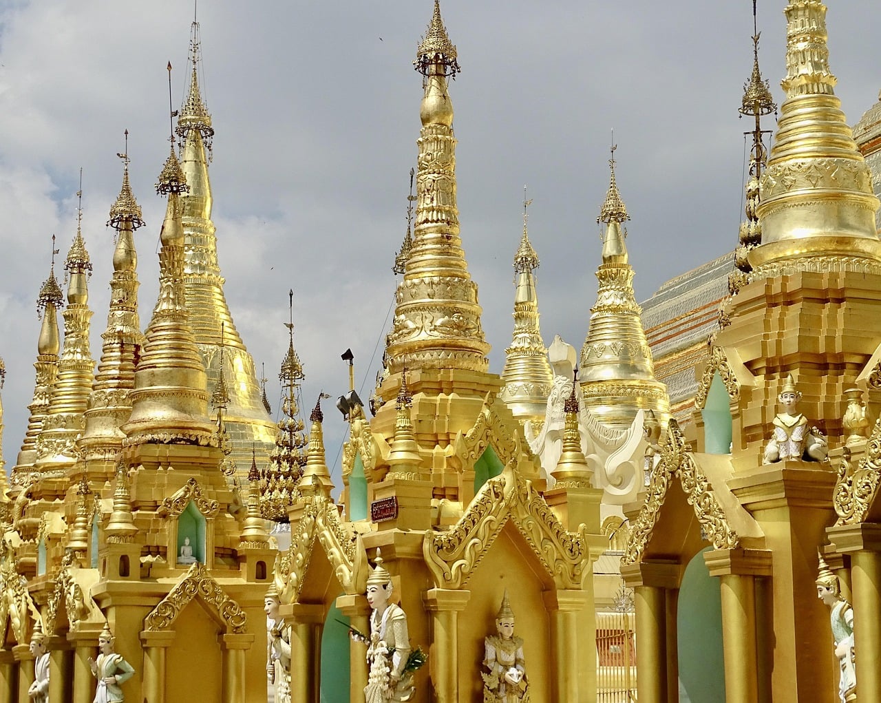 A dense cluster of small gilded stupas, spires and shrine roofs surrounds Shwedagon's main stupa, with carved guardian figures at their corners.