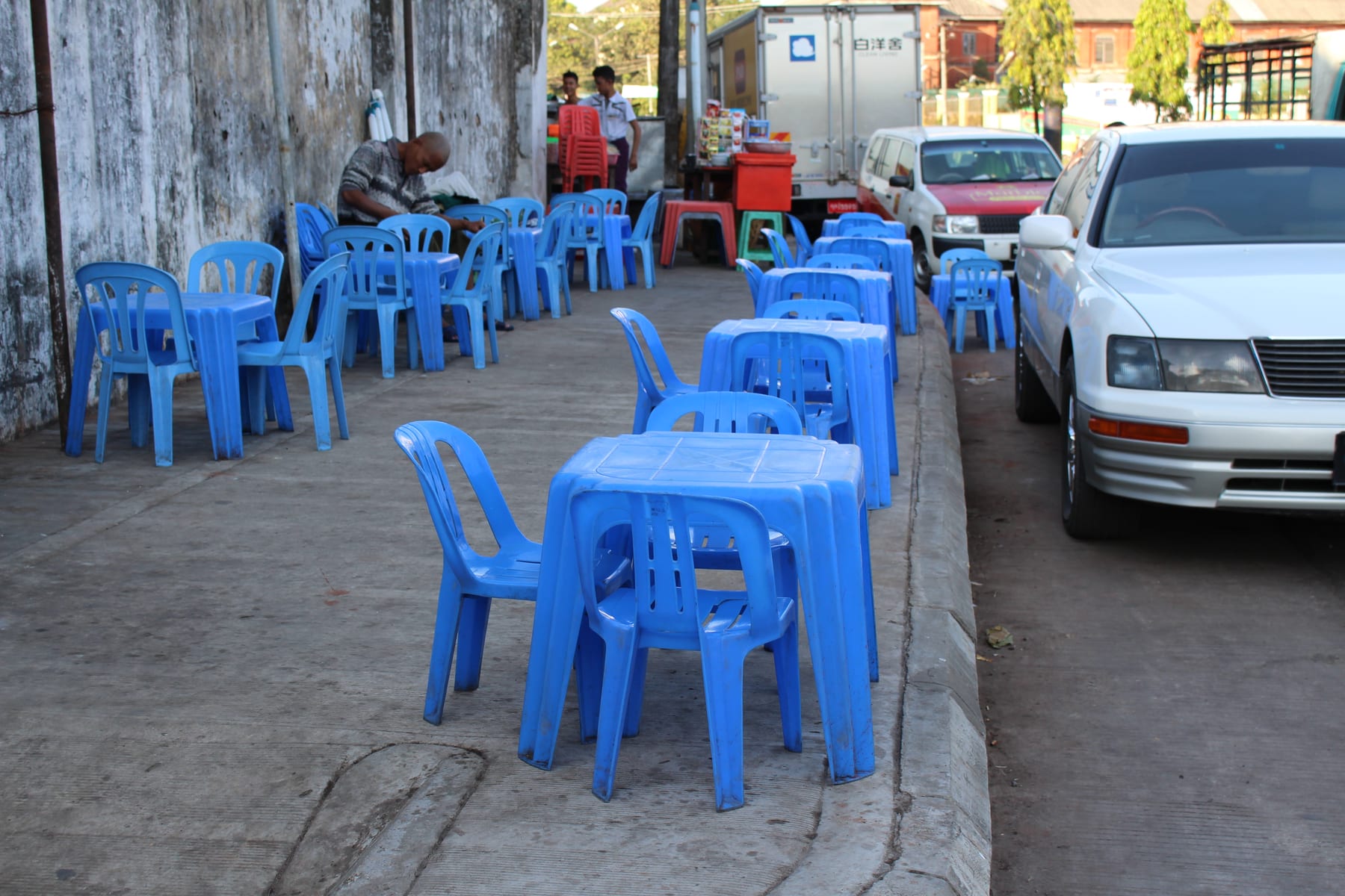 Rows of small blue plastic tables and stools set out on a Yangon pavement teashop.