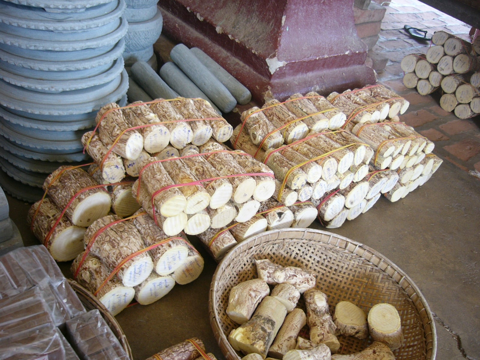 Bundles of cut thanaka logs, tied and labelled, piled beside baskets of smaller pieces for sale.