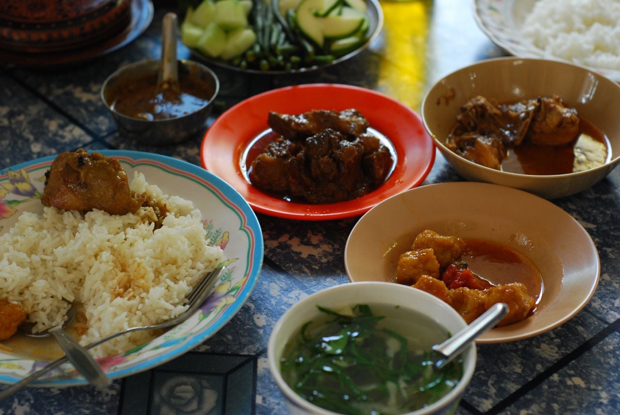 A home table set with several small dishes of curry, soup, vegetables and rice, ready to share.