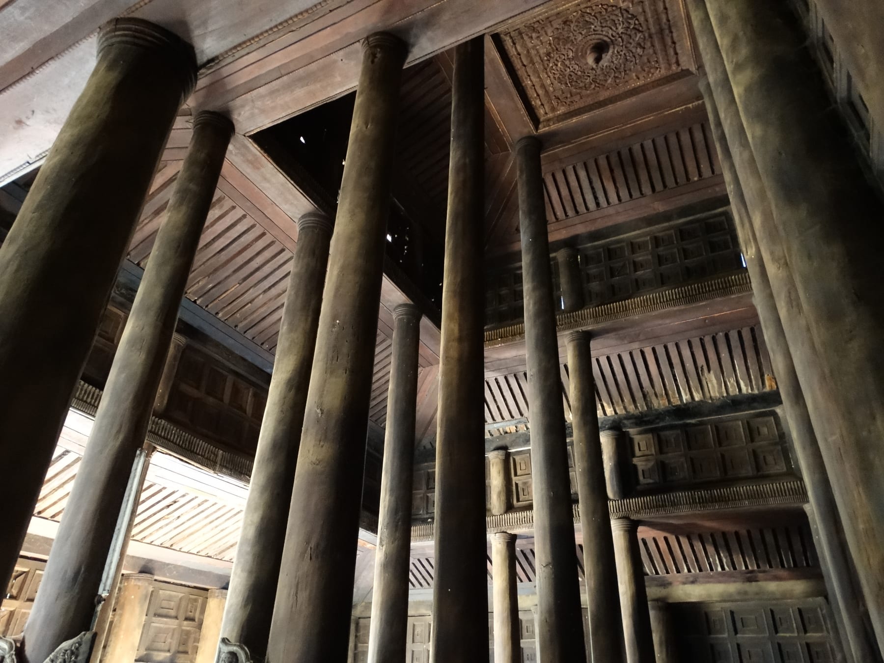 A view looking up at the massive carved teak pillars and ceiling inside Bagaya Monastery.