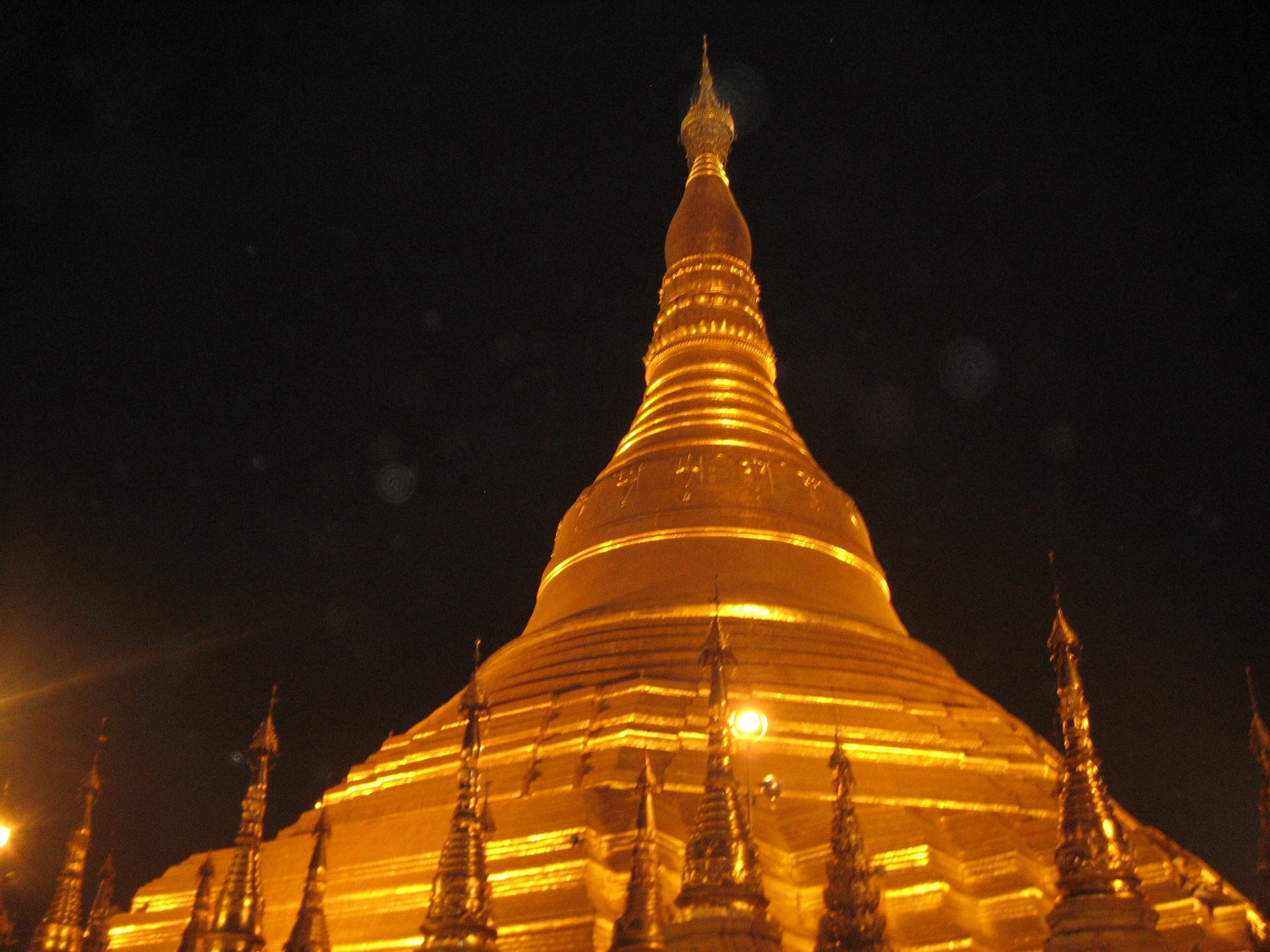 The golden spire of Shwedagon Pagoda's stupa, illuminated against a black night sky.