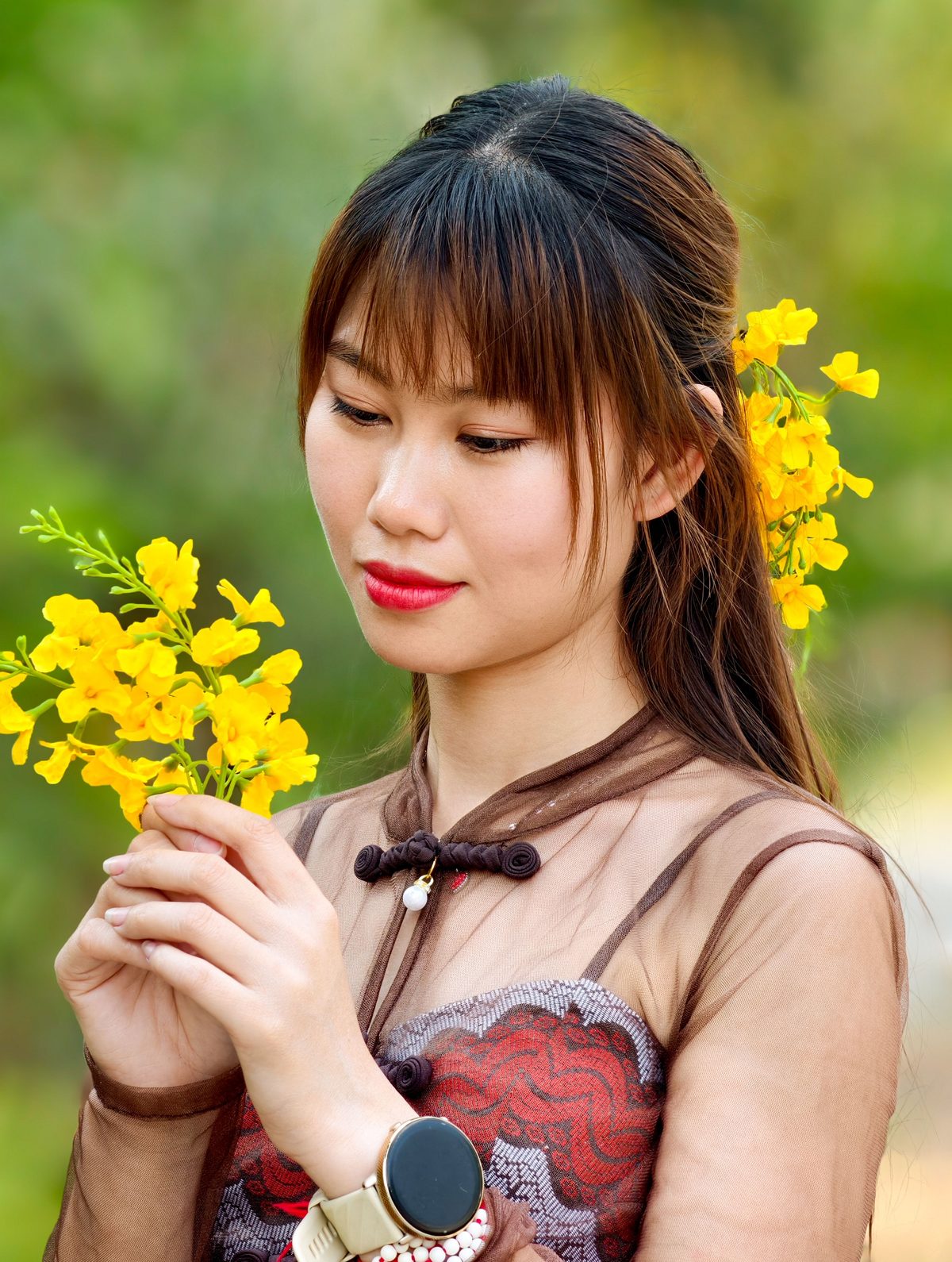 A young woman in traditional dress holds a sprig of golden-yellow padauk blossoms, with more tucked into her hair.