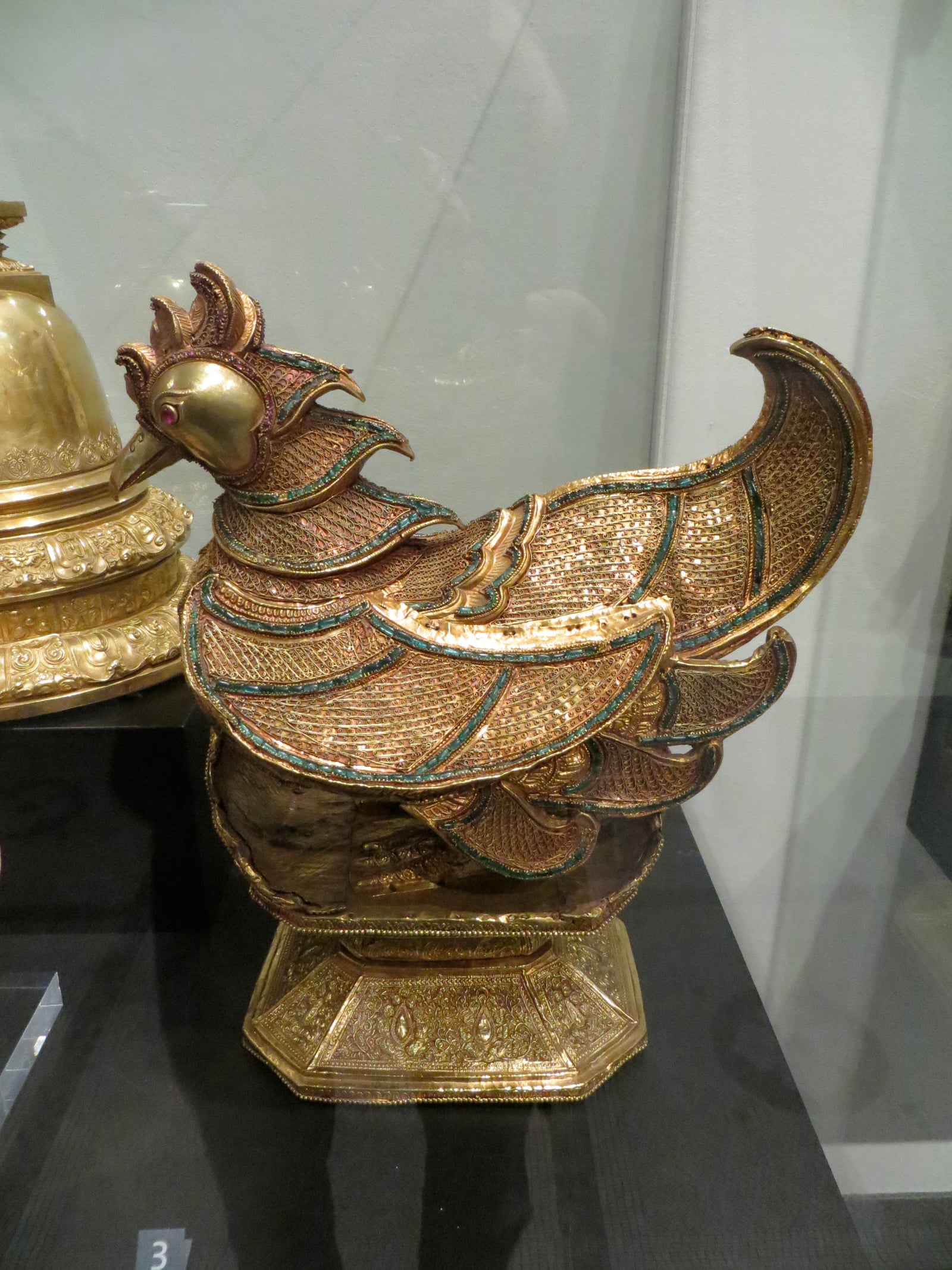 A gold betel container shaped as a mythical karaweik bird, its feathers worked in fine filigree and set with coloured stones.
