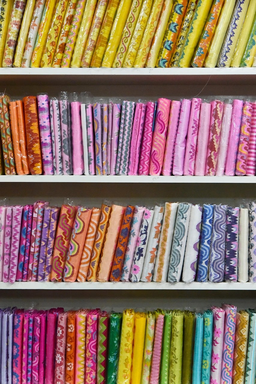 Shelves stacked with rolls of brightly coloured Burmese fabric in yellow, pink, orange and blue, each with its own woven pattern.