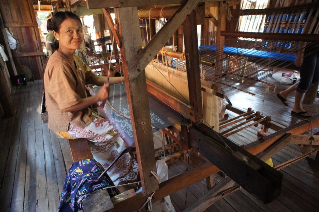 A woman weaves lotus-fibre cloth on a wooden loom inside a stilt house at Inle Lake.