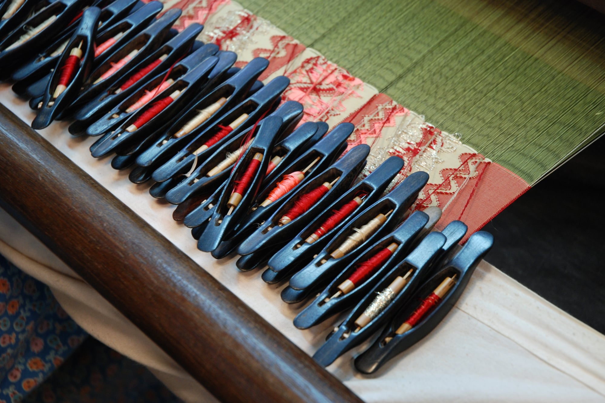 Dozens of small wooden shuttles, each wound with a different coloured thread, laid across a loom in a row.