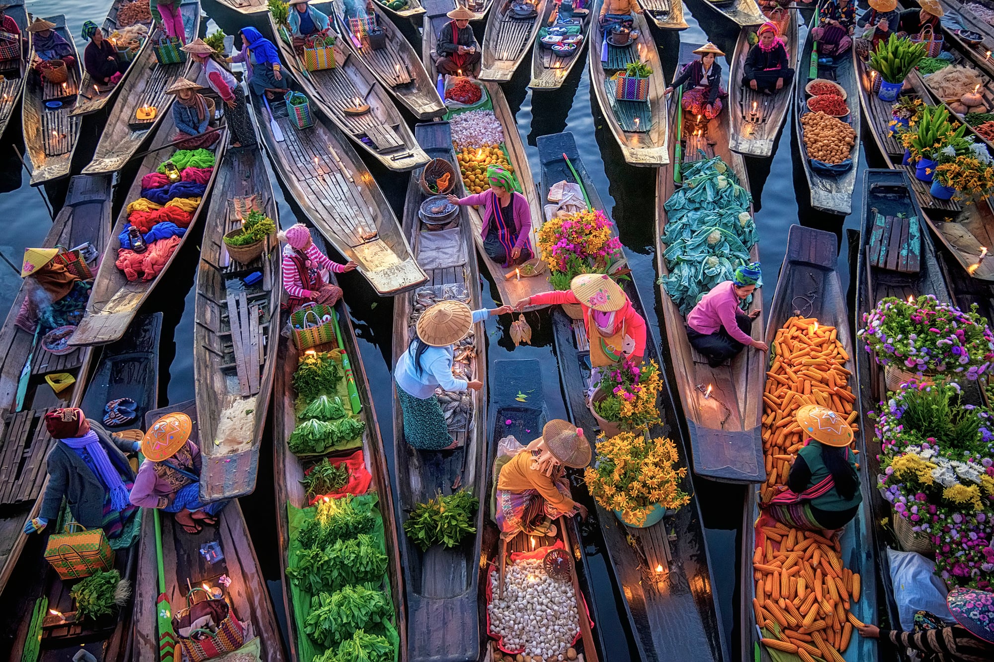 An overhead view of narrow wooden boats loaded with vegetables, flowers and goods, moored together at a floating market on Inle Lake.