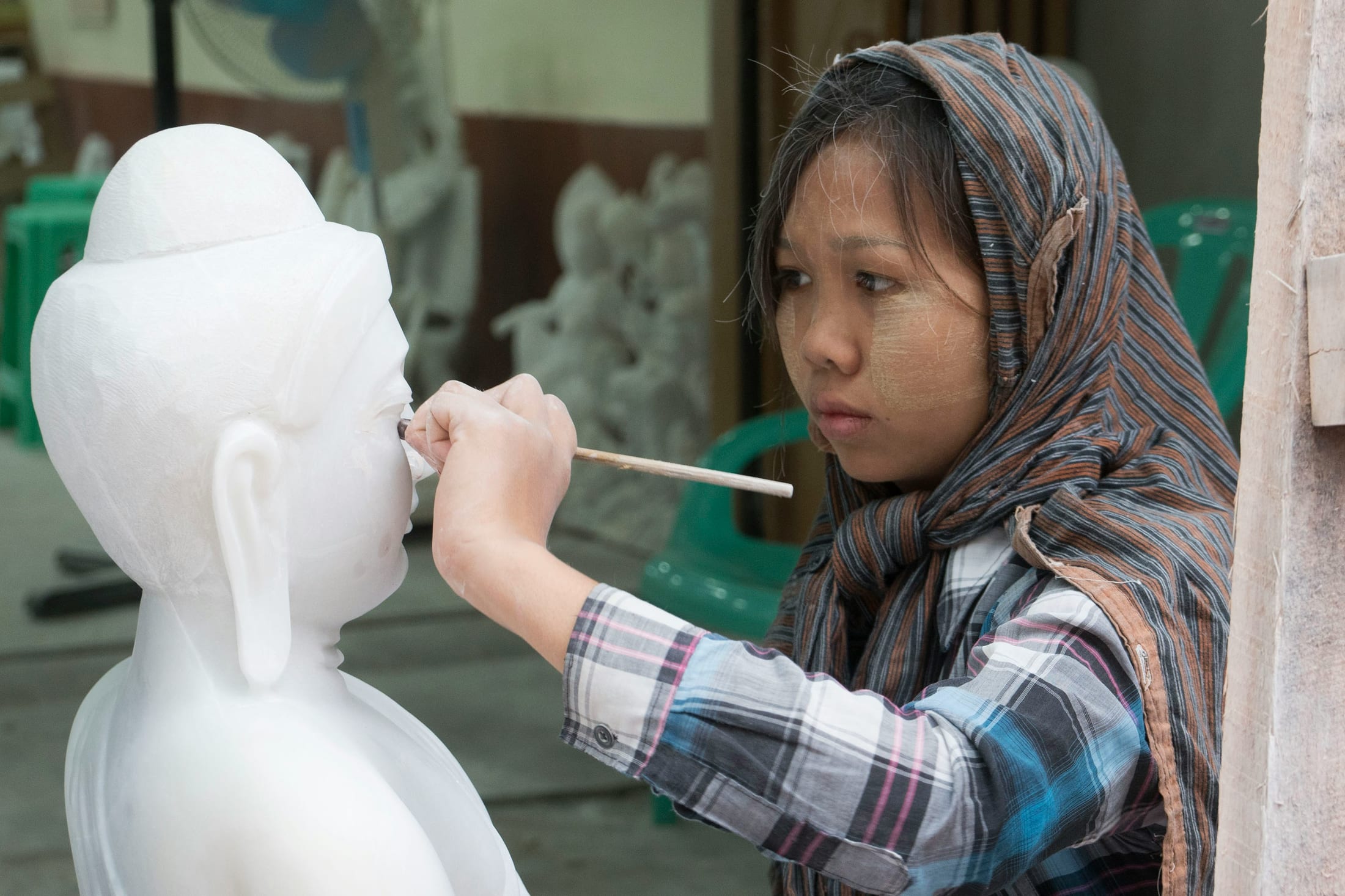 A craftswoman carving and painting a marble Buddha image in a Mandalay workshop