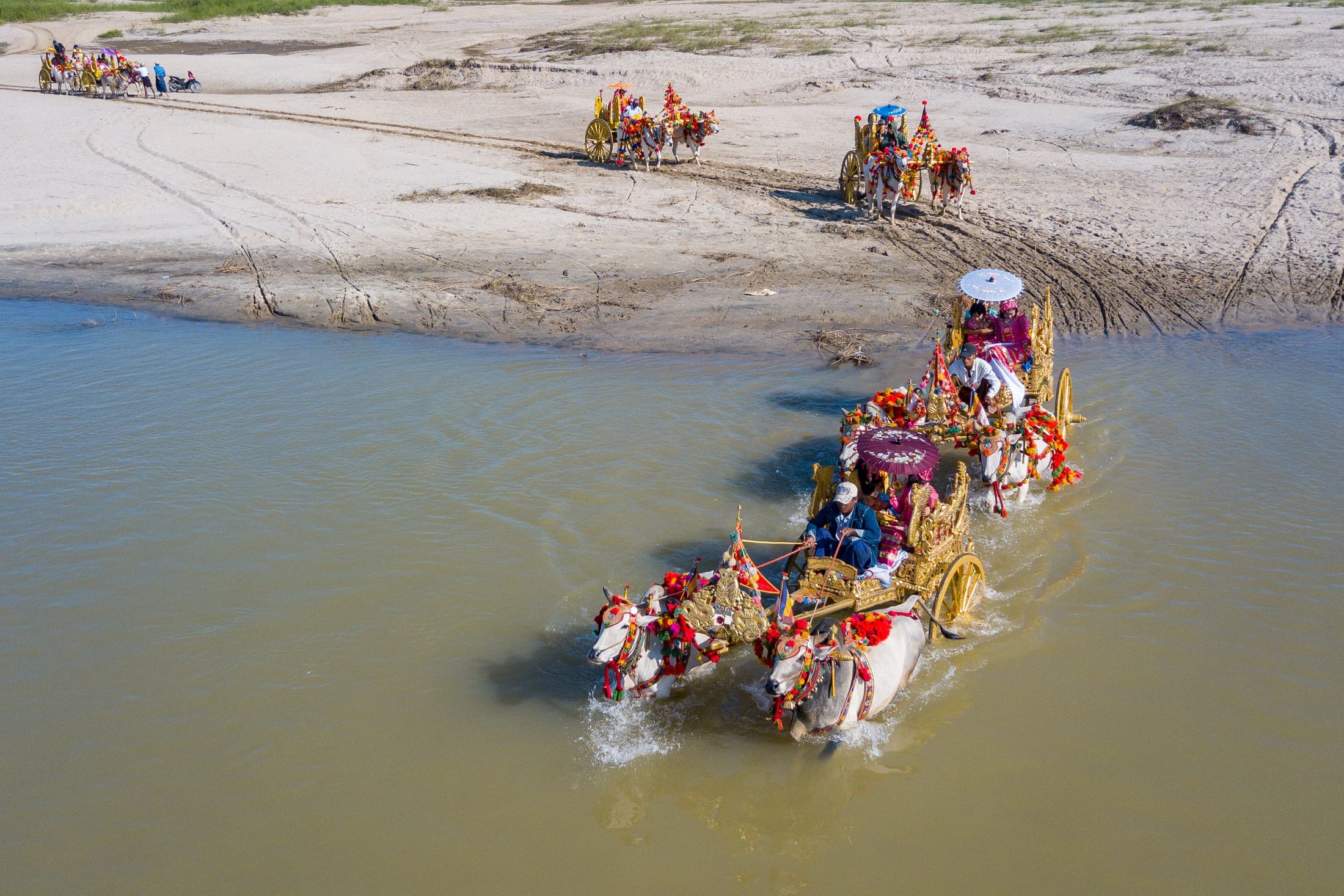 Aerial view of gilded ceremonial ox carts crossing a river during a traditional procession near Mandalay