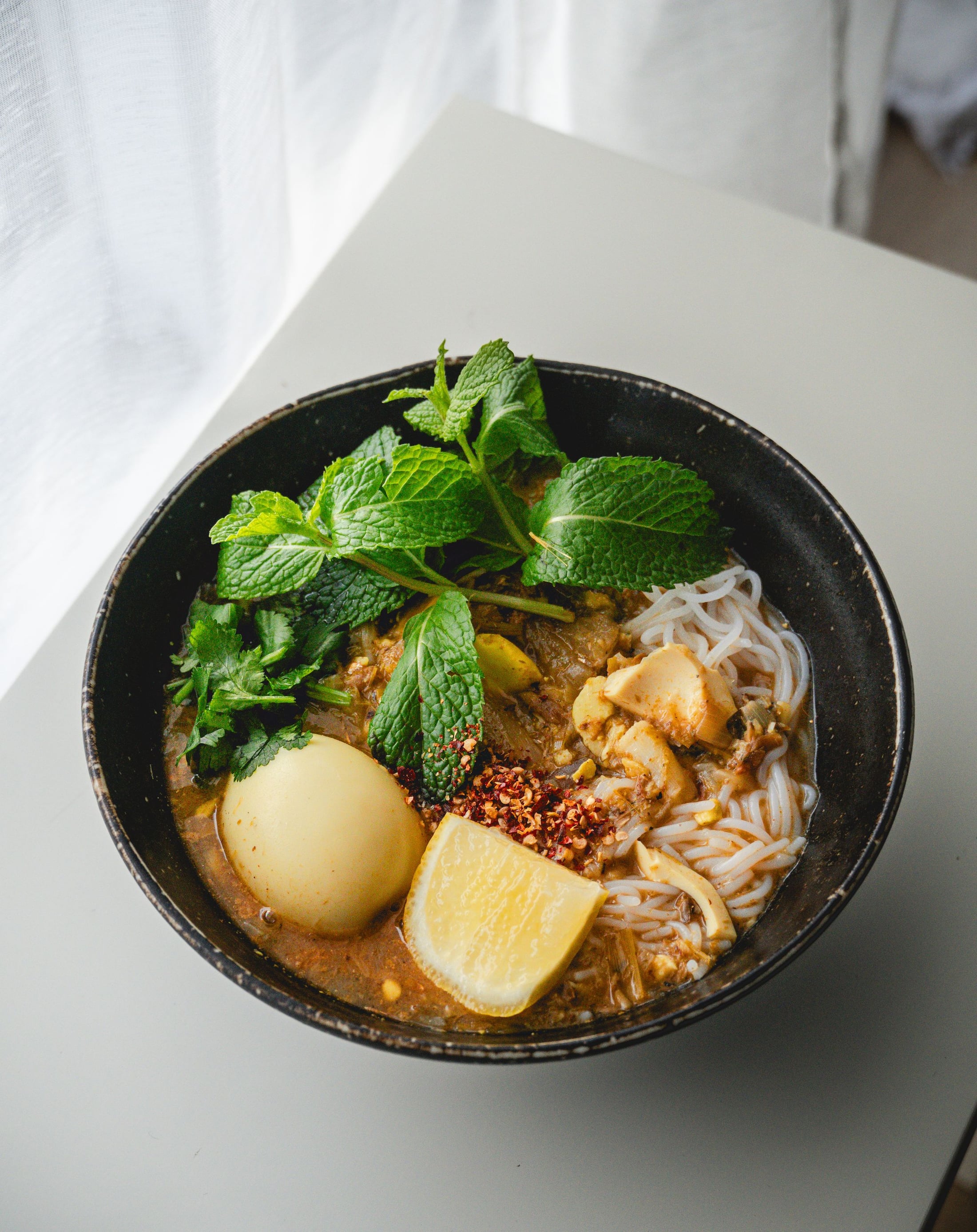 A bowl of mohinga, Myanmar's classic fish noodle soup, topped with fresh mint, a boiled egg and a wedge of lime